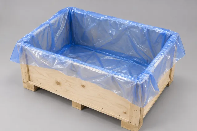 Blaue transparente Innenhülle in einem offenen Holztransportkasten; die Folie ist über den Rand umgelegt.