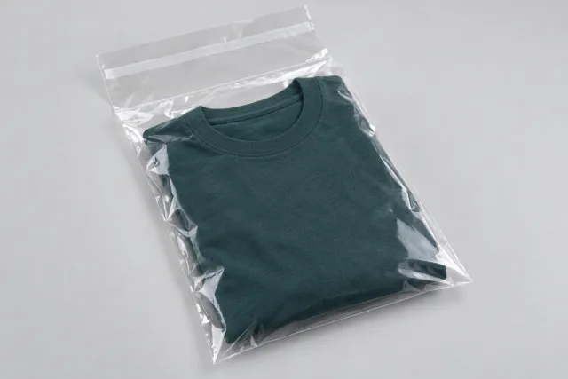 Gefaltetes petrolfarbenes Textil in einem klaren Klappenbeutel; die offene Klappe trägt einen weißen Abdeckstreifen.