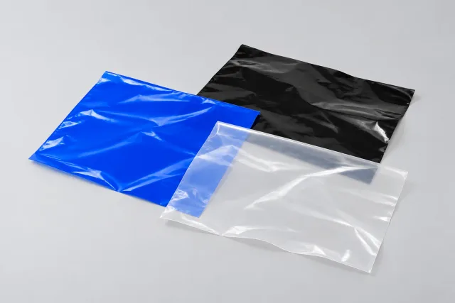 Blaue, schwarze und transparente dünne Folienmuster liegen leicht überlappend auf einer hellgrauen Fläche.