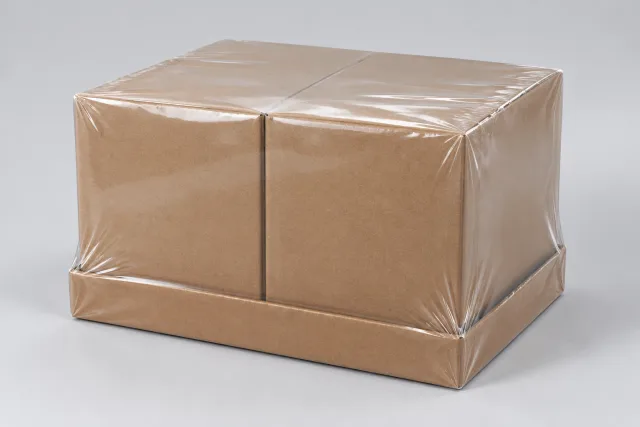 Zwei neutrale braune Kartons stehen in einem niedrigen Tray unter einer durchgehenden transparenten Folienhülle.