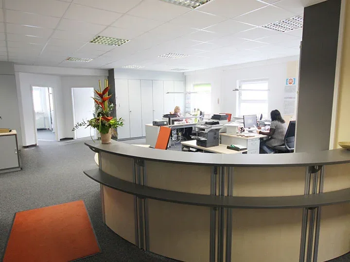 Büro mit gebogenem Empfangstresen und zwei besetzten Arbeitsplätzen.