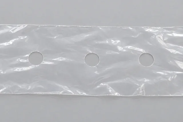 Flachliegende transluzente Folienprobe mit drei runden Durchbrüchen, durch die der graue Untergrund sichtbar ist.